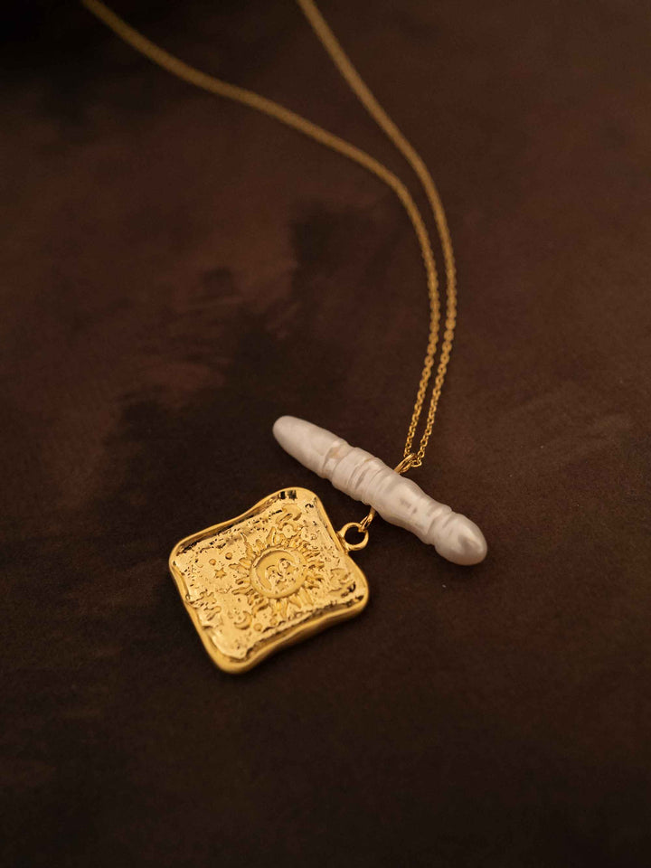 A gold necklace with square pendants and baroque pearls