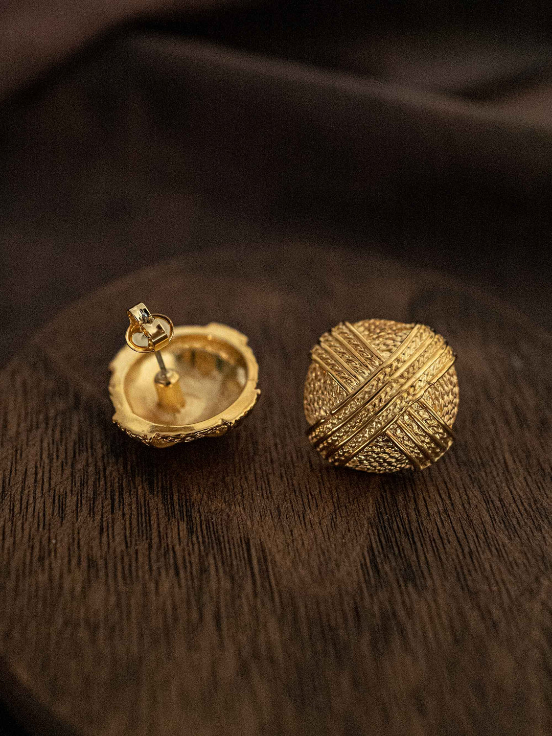 A round gold earring with a criss-cross pattern